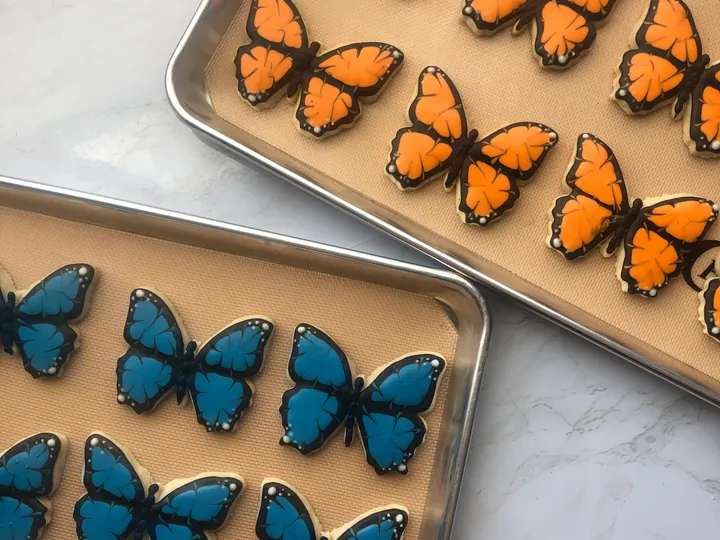 Custom orange and blue butterfly cookies arranged on baking trays